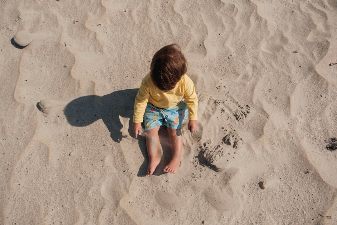 A toddler sitting and playing on clean, pale beach sand