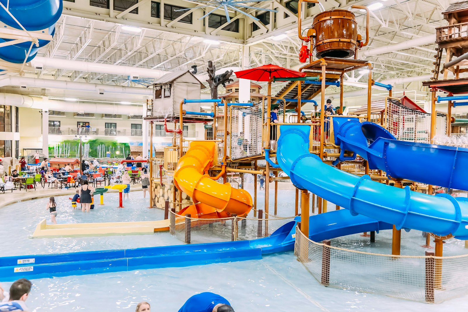 Large indoor hotel waterpark with slides and splash play structures, families in the water