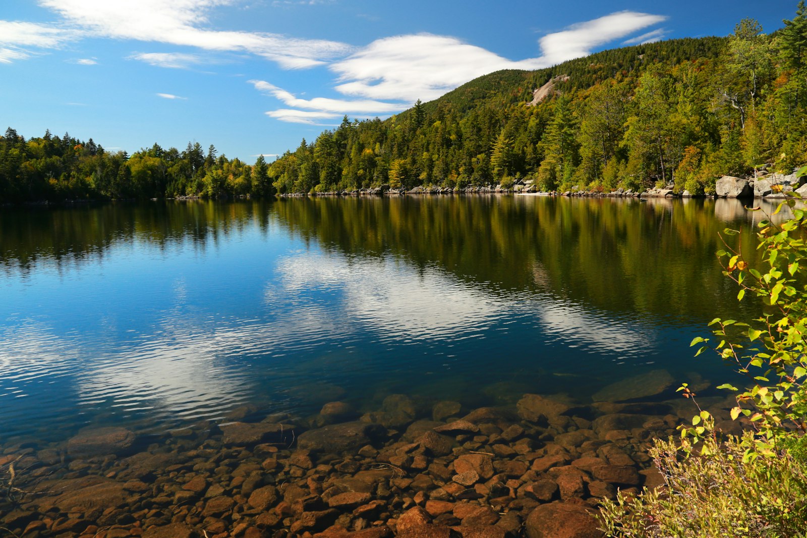 Crystal clear Adirondack lake in New York with a forested mountain and a shallow pebbled shoreline