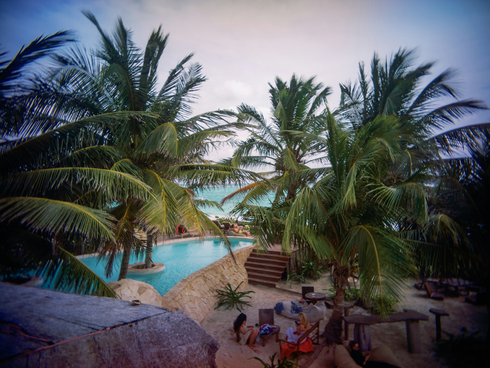 Resort swimming pool ringed by coconut palms with a white sand beach and turquoise water beyond