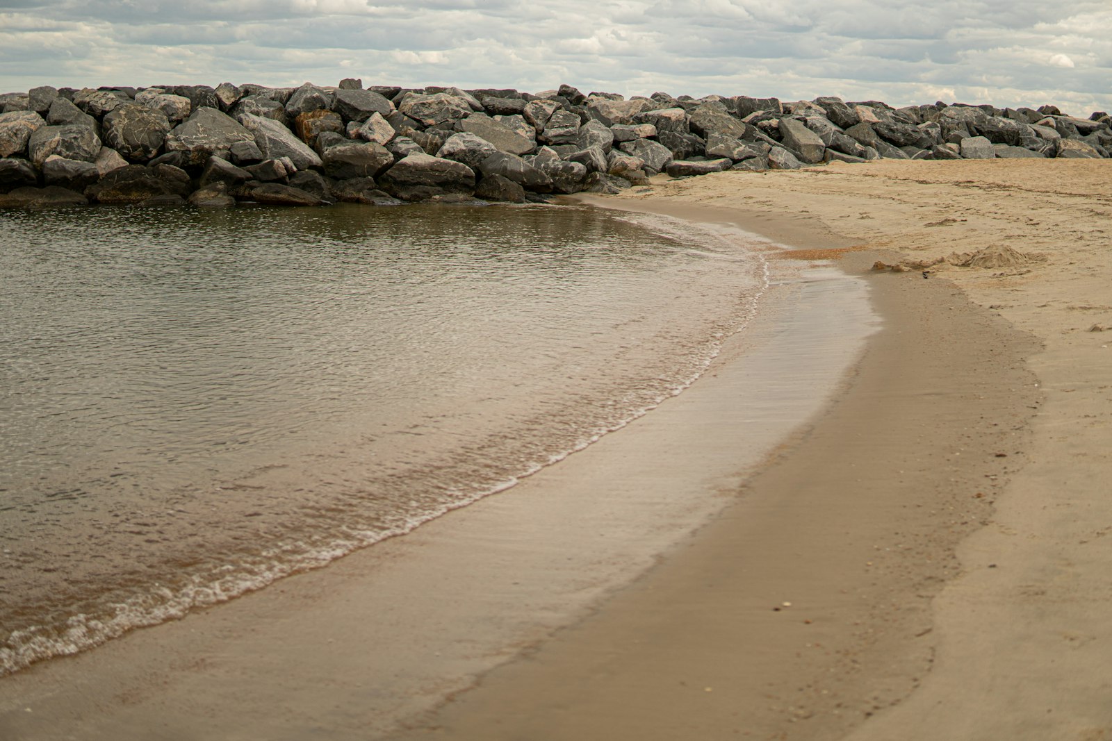 Calm sandy tidewater beach in coastal Virginia with a rock breakwater and shallow water